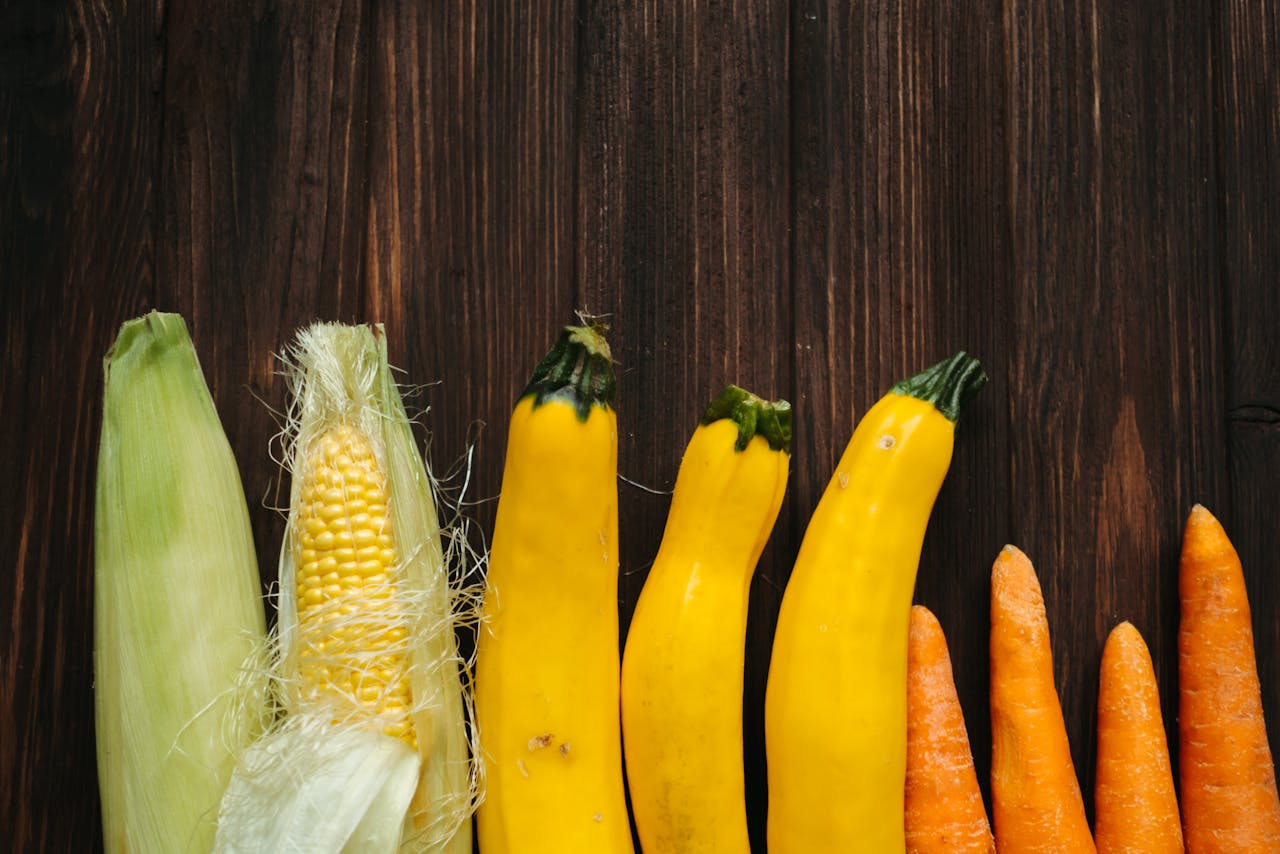 Colorful fresh corn, zucchini, and carrots arranged on a rustic wooden background.