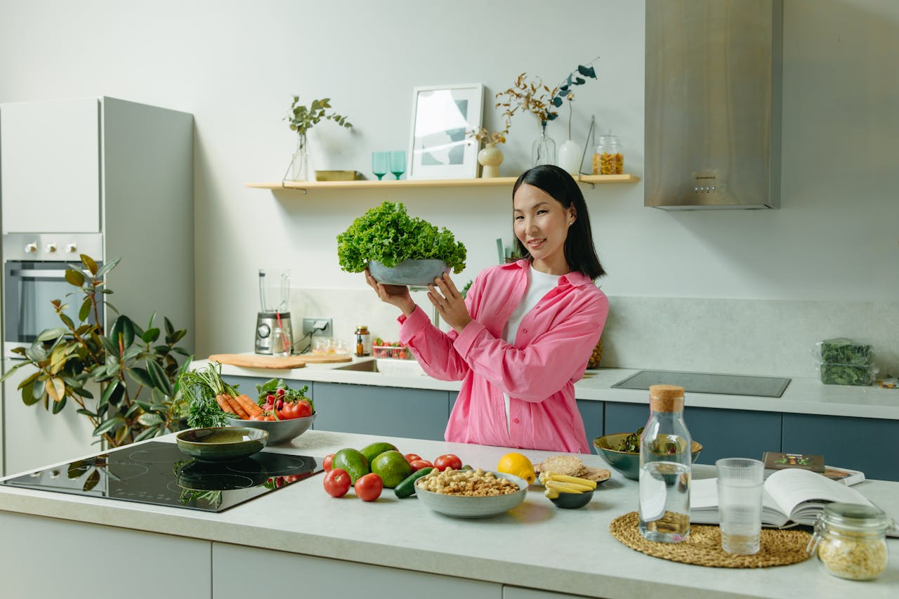 heros-img Woman in a kitchen holding fresh lettuce, surrounded by healthy ingredients like tomatoes and avocados, promoting healthy eating.
